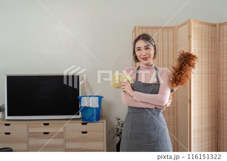Housekeeper Smiling While Holding Cleaning Tools in a Modern Living Room Setting 116151322