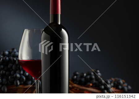 Bottle and glass of red wine with blue grapes on a black background. 116151342