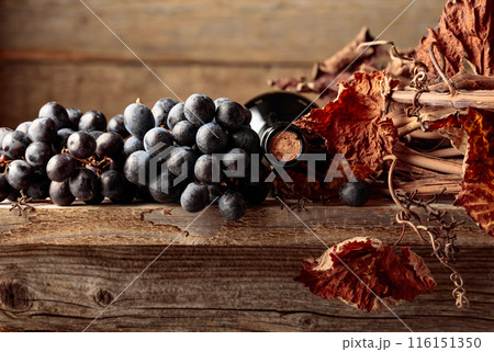 Bottle of red wine with grapes and dried vine on an old wooden table. Bottle of red wine with grapes and dried vine on an old wooden table. 116151350