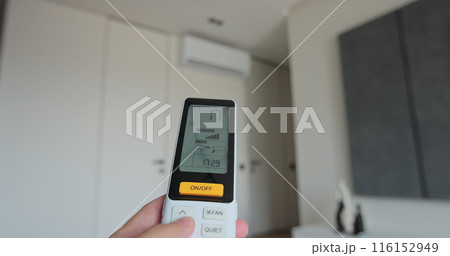 Man adjust the temperature on air conditioner in the living room. Hand uses air conditioner remote control. 116152949