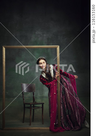 Portrait of curious elegant young woman, royal person peek out picture frame with interest against dark green background. Portrait of curious elegant young woman, royal person peek out picture frame with interest against dark green background. 116153160