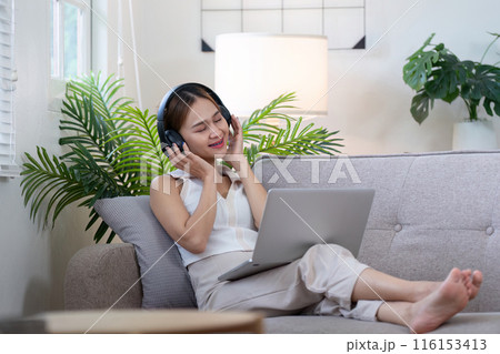Young Woman Relax on Sofa with Headphones and Laptop, Enjoying Music in Modern Cozy Living Room Young Woman Relax on Sofa with Headphones and Laptop, Enjoying Music in Modern Cozy Living Room 116153413