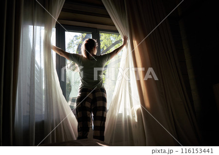 Woman Drawing Curtains to Bright Morning Sunlight 116153441