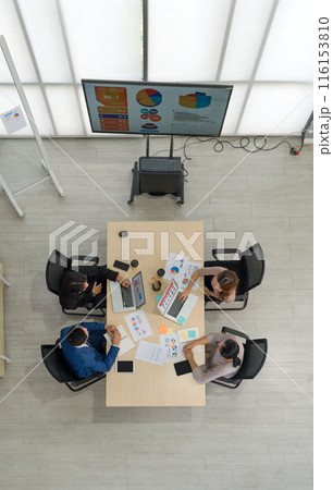 A team of worker is seated together at a big table in an office, sharing thought and talking. Top view 116153810