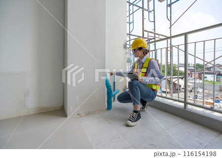 A construction worker is inspecting a building site. They are wearing safety gear and checking plumbing installation indoor. A construction worker is inspecting a building site. They are wearing safety gear and checking plumbing installation indoor. 116154198