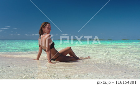 Woman relax on Maldives sitting tropic sand beach. Crystal turquoise water, white sand, blue sky, sunny day. Caucasian female in bikini enjoy outdoor lifestyle travel on summer holiday vacation. 116154881