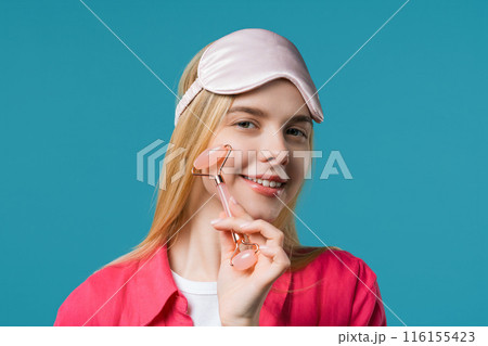 Young woman with rose quartz stone roller on blue background. Facial self care 116155423