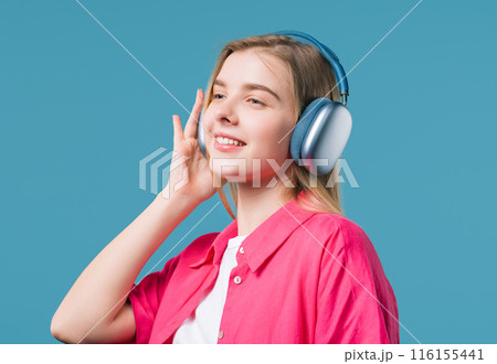 Blonde 20s woman listening streaming music, dancing with headphones on blue Blonde 20s woman listening streaming music, dancing with headphones on blue 116155441