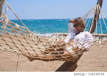 Enjoying summer vacation. Young happy woman relaxing while lying in the hammock on the sandy beach 116156529