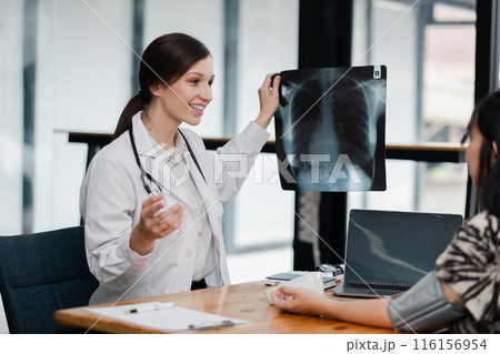 A female doctor showing and explaining X-ray results to a patient in a contemporary medical office setting. 116156954