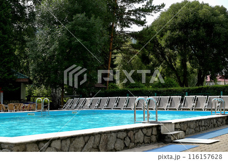 Shiny stainless steel swimming pool handrails next to the blue swimming pool The edge of the pool floor is covered with smart boards. There are many beds and pool chairs. 116157628