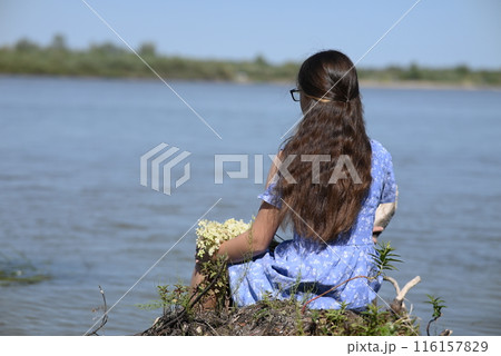 A young girl with long dark hair stands on the bank of the river. A young girl with long dark hair stands on the bank of the river. 116157829