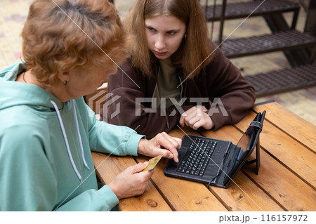 computer awareness of the elderly. a happy teenage girl teaches older 70s grandmothers to use a laptop at home. social media and modern technologies 116157972