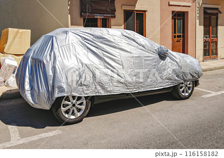 Vehicle parked on the street, fully covered with a protective silver tarp. UV and heat automotive outdoor protection concept 116158182