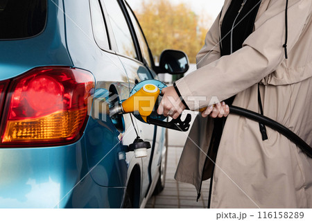 Attractive young woman refueling car at gas station. Female filling diesel at gasoline fuel in car using a fuel nozzle. Petrol concept. Side view 116158289