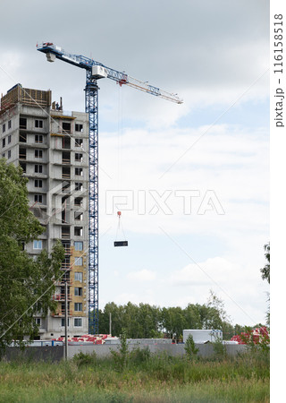 View of the unfinished wall of the house. A construction crane on a blue sky background. View of the unfinished wall of the house. A construction crane on a blue sky background. 116158518