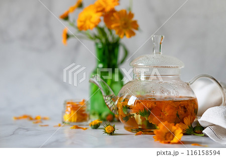Cup of marigold tea and calendula flowers outdoors on green background. Cup of marigold tea and calendula flowers outdoors on green background. 116158594