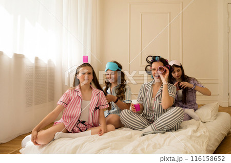 Girls and mom play with curlers in a cozy bedroom. 116158652