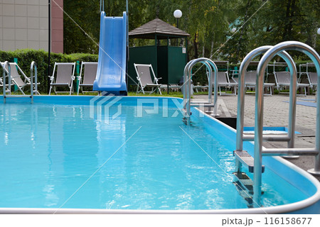 Shiny stainless steel swimming pool handrails next to the blue swimming pool The edge of the pool floor is covered with smart boards. There are many beds and pool chairs. Shiny stainless steel swimming pool handrails next to the blue swimming pool The edge of the pool floor is covered with smart boards. There are many beds and pool chairs. 116158677