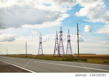 High voltage power lines leading through a green field. Transmission of electricity by means of supports through agricultural areas. 116158787