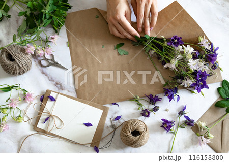 Marble desk with pink and blue flowers, postcard, kraft envelope, twine, cotton branch. Layout of Women's Day or Mother's Day, St. Valentine's Day, flat position, top view. 116158800