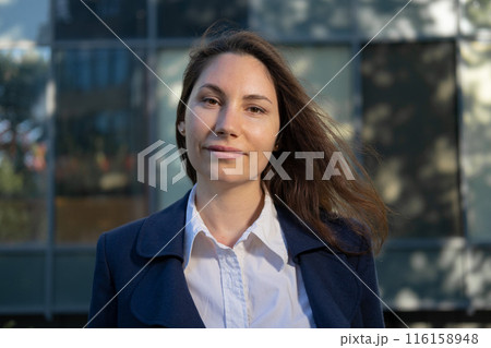 Portrait of an attractive strong confident independent woman in a blue suit standing against the background of a business building and looking at the camera Portrait of an attractive strong confident independent woman in a blue suit standing against the background of a business building and looking at the camera 116158948