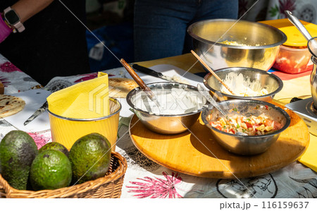 Sauces table, metal bowls, creamy sauce, salsa, wooden board, basket avocados, kitchen utensils 116159637