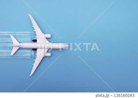 A plane model with a medical mask on a blue background. Safety flight and travel during quarantine and lockdown. Safe travels concept. Opening borders A plane model with a medical mask on a blue background. Safety flight and travel during quarantine and lockdown. Safe travels concept. Opening borders 116160263