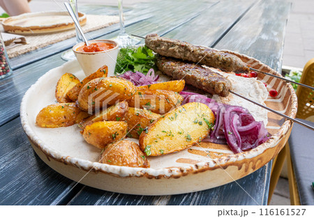 Georgian lula kebab with baked potatoes, sauce and greens. Grilled souvlaki, minced meat kebap, lamb on skewers 116161527