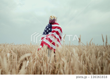 Unrecognizable woman standing with american stars and stripes national flag in rural wheat field landscape. USA, 4th July celebration, US banner, memorial Veterans, election, America, labor 116161818