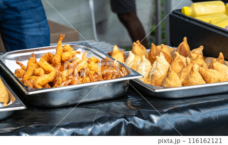 Assorted Asian street food in stainless steel trays, fried squid, various dumplings, spring rolls at food market 116162121