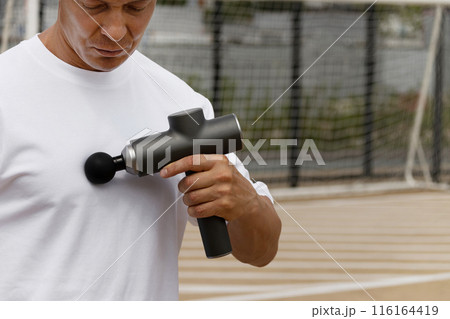 Sports man massaging chest muscles. Massage gun for athletes, handheld cordless professional percussion deep tissue body muscle fascia. Close up. Copy space. 116164419