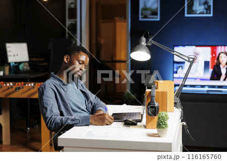 Accounting manager takes notes on papers after calculating budget with expenses and profit, doing online analysis from home. Specialist writing important financial details on notebook. 116165760