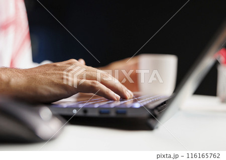 Selective focus on hands of a Middle Eastern individual typing and taking notes on a minicomputer while remaining wirelessly connected. Close-up of a person using a contemporary digital laptop. Selective focus on hands of a Middle Eastern individual typing and taking notes on a minicomputer while remaining wirelessly connected. Close-up of a person using a contemporary digital laptop. 116165762