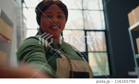 African american warehouse employee using selfie smartphone camera to participate in online videocall with management executives. Worker in teleconference meeting with distribution center managers 116165798