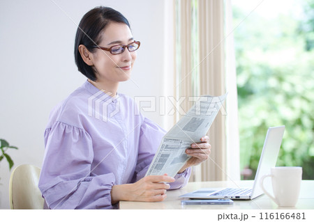 老眼鏡を掛けて英字新聞を読むミドル女性 116166481