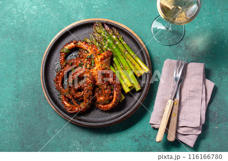 Grilled octopus with asparagus served on a black plate, highlighting vibrant colors and textures against a turquoise background. Grilled octopus with asparagus served on a black plate, highlighting vibrant colors and textures against a turquoise background. 116166780