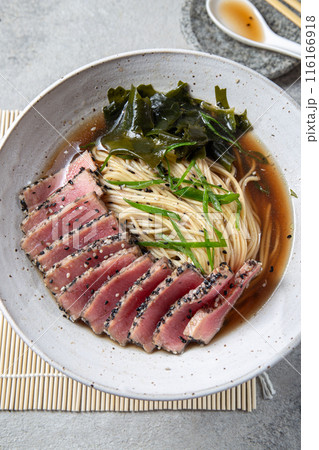 A bowl of ramen featuring perfectly seared tuna slices, garnished with fresh greens, seaweed, and served in a savory broth. A bowl of ramen featuring perfectly seared tuna slices, garnished with fresh greens, seaweed, and served in a savory broth. 116166918
