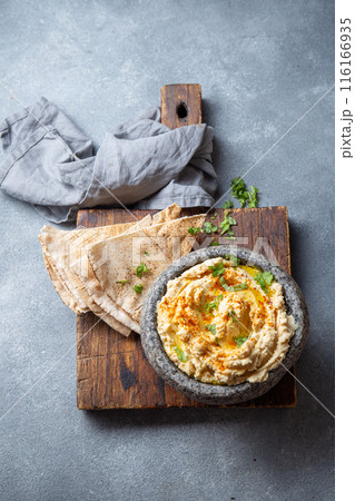 Traditional Jewish hummus served in a stone bowl, garnished with olive oil, paprika, and parsley, alongside flatbreads and fresh herbs on a gray table Traditional Jewish hummus served in a stone bowl, garnished with olive oil, paprika, and parsley, alongside flatbreads and fresh herbs on a gray table 116166935