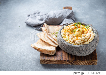 Traditional Jewish hummus served in a stone bowl, garnished with olive oil, paprika, and parsley, alongside flatbreads and fresh herbs on a gray table Traditional Jewish hummus served in a stone bowl, garnished with olive oil, paprika, and parsley, alongside flatbreads and fresh herbs on a gray table 116166938