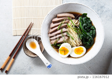 A bowl of ramen with slices of beef, soft-boiled egg halves, and green vegetables. The meal is garnished with green onions A bowl of ramen with slices of beef, soft-boiled egg halves, and green vegetables. The meal is garnished with green onions 116167012