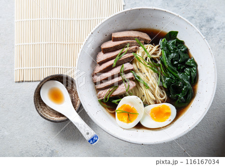 A bowl of ramen with slices of beef, soft-boiled egg halves, and green vegetables. The meal is garnished with green onions A bowl of ramen with slices of beef, soft-boiled egg halves, and green vegetables. The meal is garnished with green onions 116167034