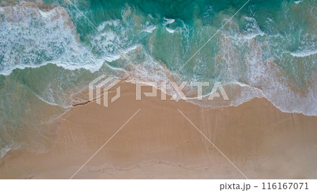 Aerial view of a sandy beach with turquoise waves crashing onto the shore, scattered people are seen walking along the coastline Aerial view of a sandy beach with turquoise waves crashing onto the shore, scattered people are seen walking along the coastline 116167071