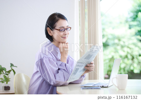 老眼鏡を掛けて英字新聞を読むミドル女性 116167132