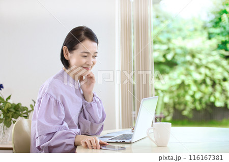 リビングでコーヒーを飲みながらパソコンを見るミドル女性 116167381