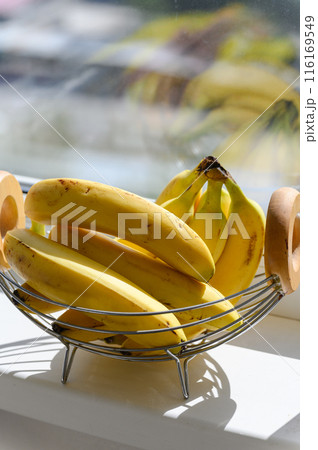 A few ripe bananas in a fruit basket stand on the windowsill. 116169549