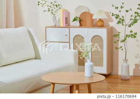Living room photography with a white sofa placed next to a wooden table contains a flower vase above, in the back is a wooden cabinet with many decorative items on top, empty space for designing 116170694