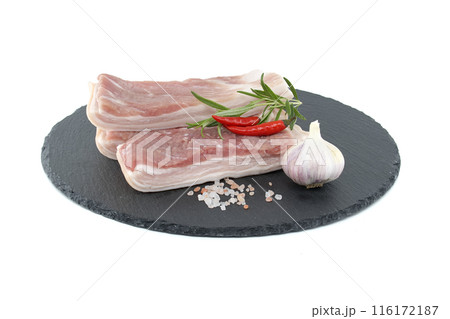 Raw pork belly slices with garlic and chili peppers on a black stone plate 116172187