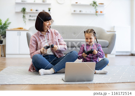 Mother and daughter playing video games together at home 116172514