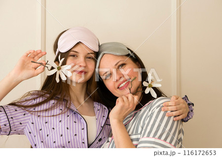 Mother and daughter in pajamas holding flowers and smiling. 116172653